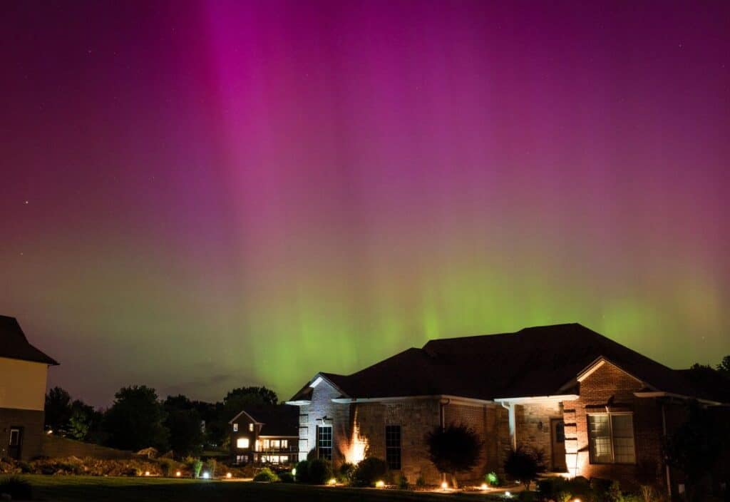 A house at night under a sky illuminated by green and purple northern lights.