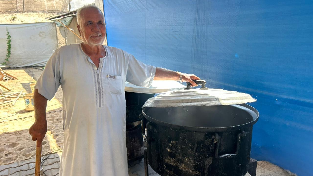 Omran Khamees Al-Astal next to a large pot for cooking with a blue tent background behind him.